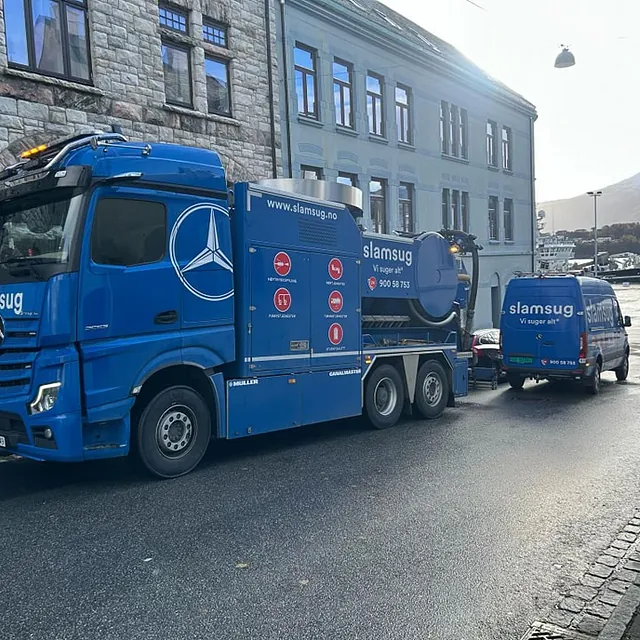 Slamsugbil og servicebil parkert ved oppdrag i bymiljø